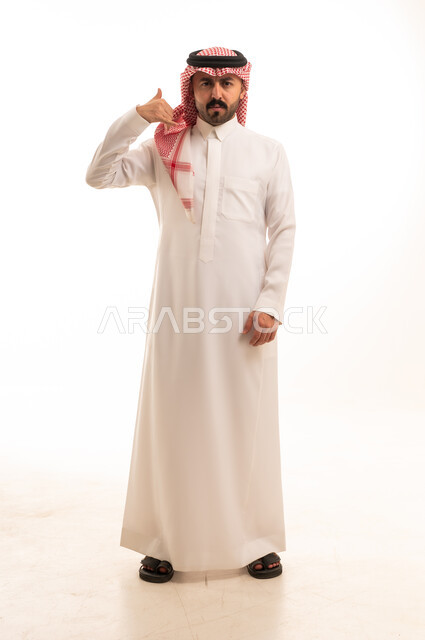 رجل سعودي بالزي التقليدي يشير بحركة الاتصال الهاتفي
