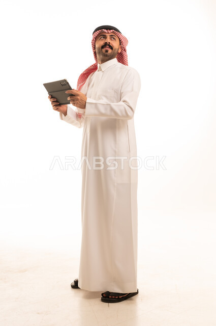رجل سعودي بالزي التقليدي يمسك جهاز لوحي رقمي بخلفية بيضاء