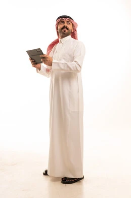 رجل سعودي بالزي التقليدي يمسك جهاز لوحي رقمي بخلفية بيضاء
