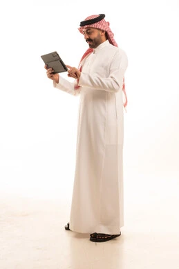 رجل سعودي بالزي التقليدي يستخدم جهازاً لوحياً