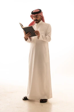 رجل سعودي يرتدي الثوب التقليدي يقرأ كتاباً في الاستوديو