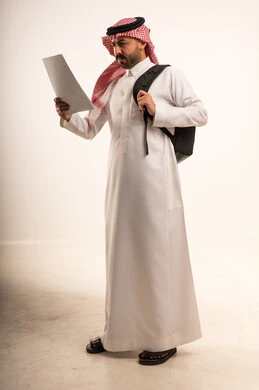 رجل سعودي بالثوب يرتدي حقيبة ظهر ويقرأ وثيقة