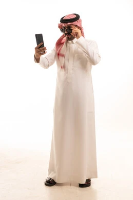 رجل سعودي بالزي التقليدي يستخدم الهاتف الذكي بخلفية بيضاء