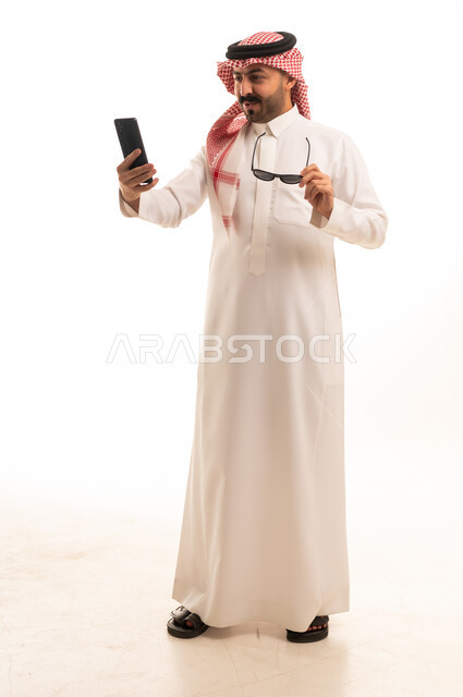 رجل سعودي بالزي التقليدي يستخدم الهاتف الذكي