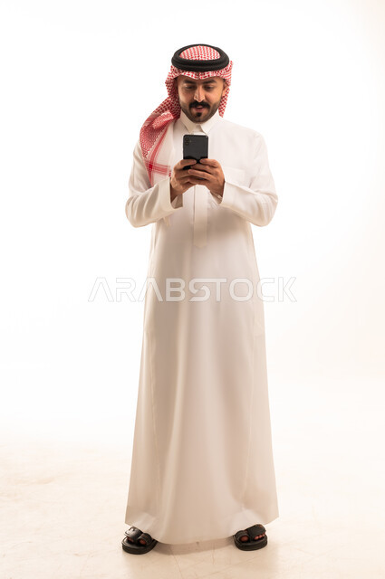 رجل سعودي بالثوب التقليدي يستخدم الهاتف الذكي