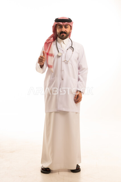 طبيب سعودي بالزي التقليدي والبالطو الأبيض يشير بالنجاح