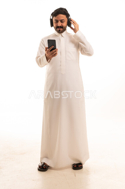 رجل سعودي بالثوب الأبيض يستخدم الهاتف وسماعات الرأس