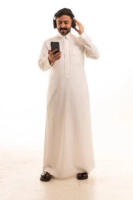 رجل سعودي بالثوب الأبيض يستخدم الهاتف وسماعات الرأس