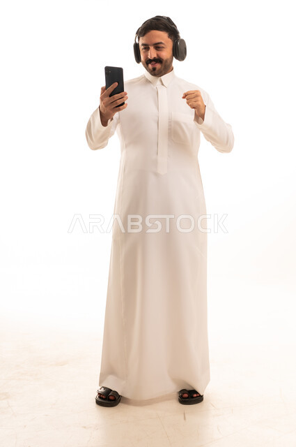 رجل سعودي بالثوب التقليدي يستخدم سماعات الرأس والجوال