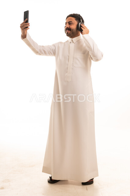 رجل سعودي بالثوب التقليدي يستخدم الهاتف والسماعات