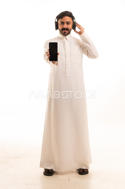 رجل سعودي بالثوب التقليدي مع سماعات وهاتف ذكي