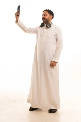 رجل سعودي بالثوب التقليدي يلتقط صورة سيلفي بالهاتف