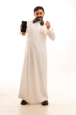 رجل سعودي بالثوب الأبيض يحمل هاتف ذكي وسماعات