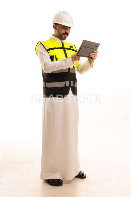 مهندس سعودي بالثوب يستخدم جهاز لوحي بخلفية بيضاء