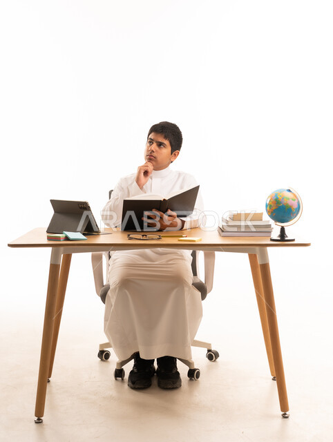 Saudi Boy in Thobe Thinking at Desk with Books
