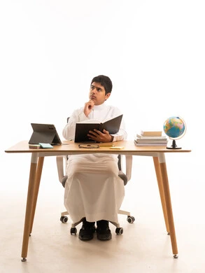 طالب سعودي بالثوب الأبيض يفكر خلف مكتب الدراسة
