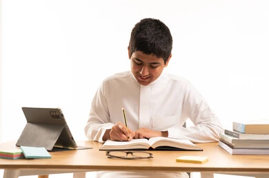 Saudi Student Writing on Desk with Tablet