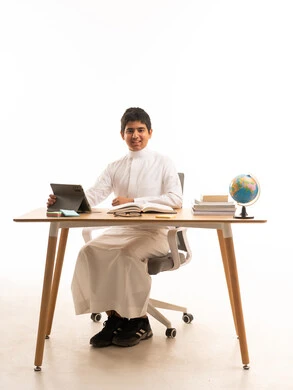 طالب سعودي على مكتب مع جهاز لوحي وكره أرضية