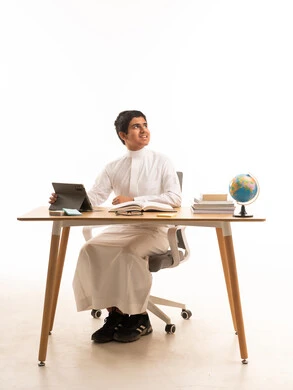 طالب سعودي يستخدم الجهاز اللوحي والكتب على مكتب الدراسة