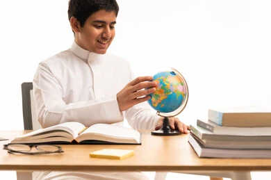 طالب سعودي بالثوب الأبيض يدرس على مجسم الكرة الأرضية