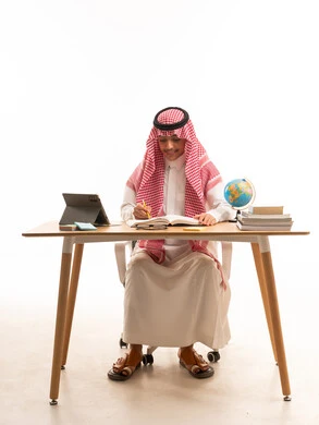 طالب سعودي يدرس على مكتب مع جهاز لوحي