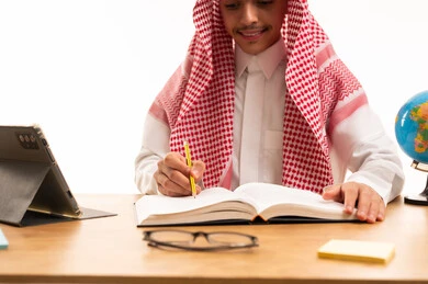 Saudi Student in Traditional Thobe Writing at Desk