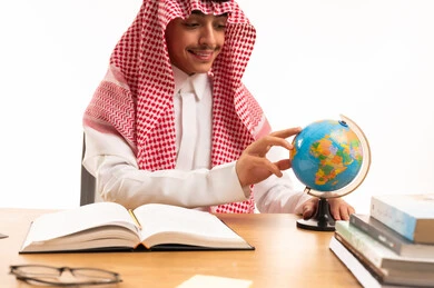 Saudi Student in Traditional Thobe Studying with Globe