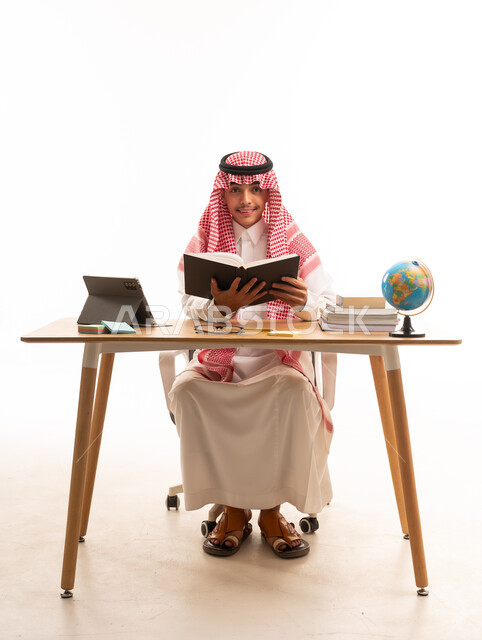 Saudi Student in Traditional Dress Reading at Desk