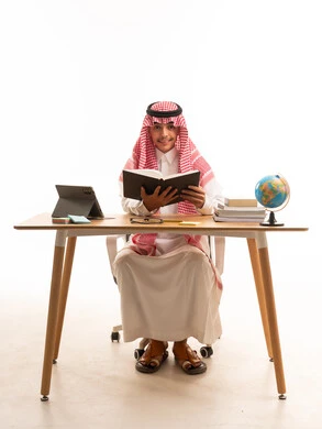 Saudi Student in Traditional Dress Reading at Desk