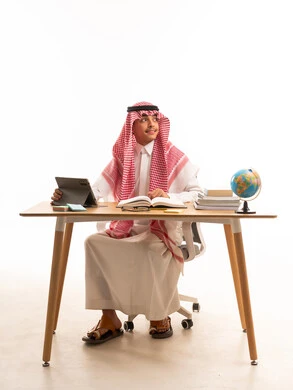 طالب سعودي يدرس على مكتب مع جهاز لوحي وكتب