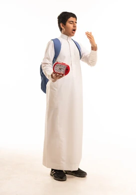 طالب سعودي يتثاءب مع ساعة منبه وحقيبة مدرسة