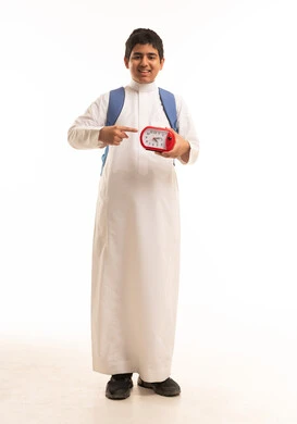 طالب سعودي يرتدي حقيبة ويحمل ساعة منبه