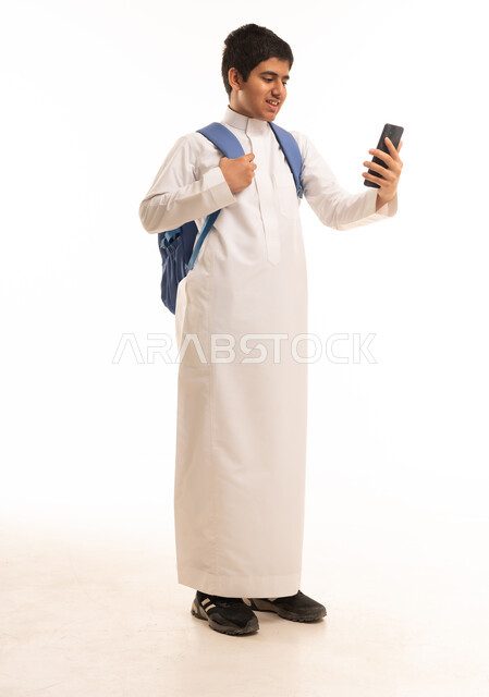 طالب مدرسي سعودي بالثوب يستخدم الهاتف الذكي
