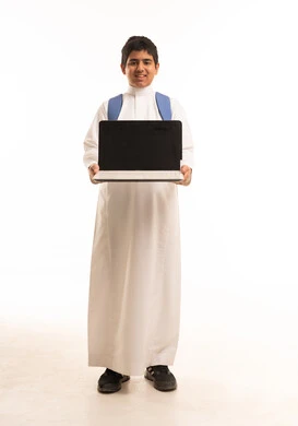 طالب سعودي يحمل لابتوب وحقيبة مدرسية أمام خلفية بيضاء