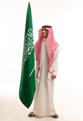 طفل سعودي بالزي التقليدي يحمل علم المملكة العربية السعودية