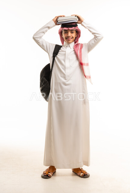 طالب سعودي بالزي التقليدي يحمل كتباً فوق رأسه