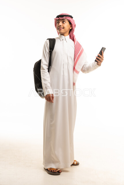 طالب سعودي يرتدي الثوب والشماغ مع حقيبة ظهر وهاتف
