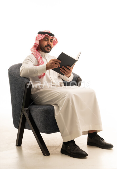 رجل سعودي بالزي التقليدي يقرأ كتاباً في الاستوديو