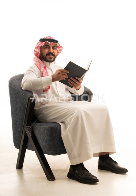 رجل سعودي بالزي التقليدي يقرأ كتاباً في الاستوديو