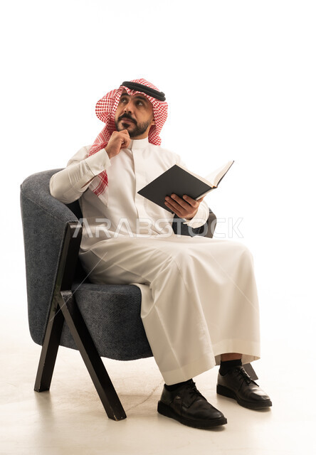 رجل سعودي بالزي التقليدي يقرأ كتاباً في استوديو