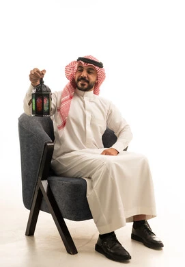 رجل سعودي يجلس مع فانوس رمضان بخلفية بيضاء