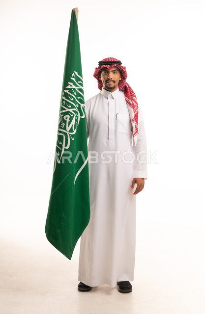 رجل سعودي بالزي التقليدي يحمل علم السعودية