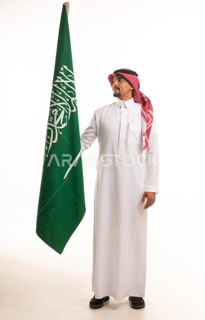 رجل سعودي بالزي التقليدي مع علم المملكة العربية السعودية