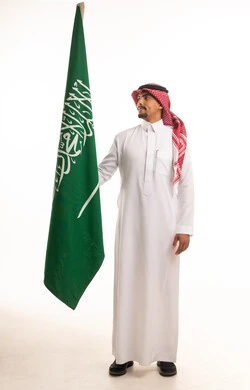 رجل سعودي بالزي التقليدي مع علم المملكة العربية السعودية