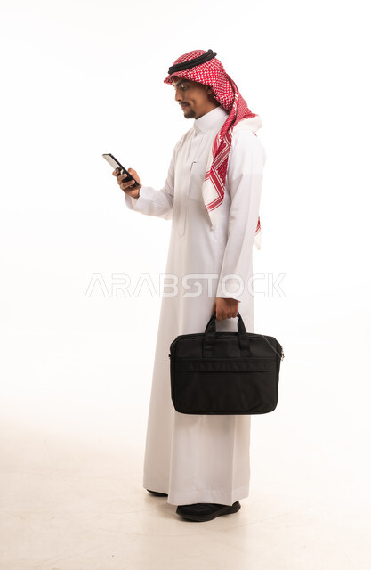 رجل أعمال سعودي بالزي التقليدي يستخدم الهاتف الذكي