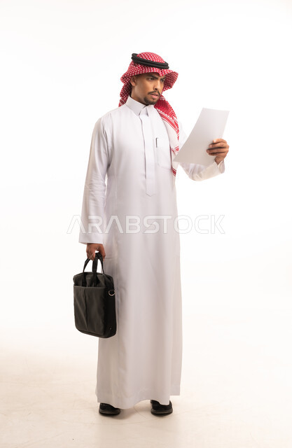 رجل أعمال سعودي يرتدي الثوب ويقرأ ورقة عمل