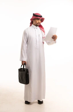 رجل أعمال سعودي يرتدي الثوب ويقرأ ورقة عمل