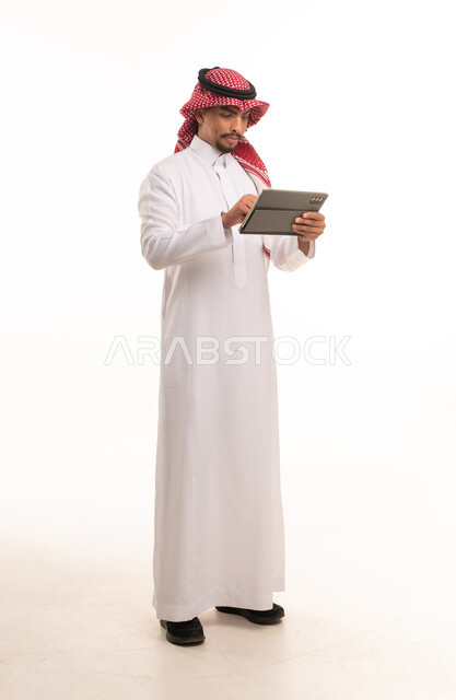 رجل سعودي بالزي التقليدي يستخدم جهازاً لوحياً