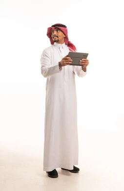 رجل سعودي بالزي التقليدي يحمل جهاز لوحي ذكي