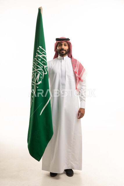 رجل سعودي بالزي التقليدي يرفع علم المملكة العربية السعودية